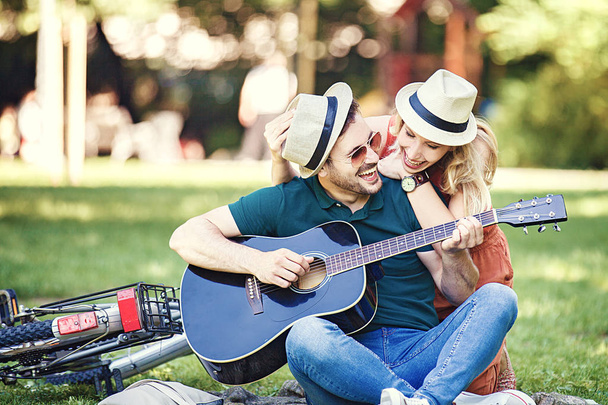Couple of romantic lovers sitting in the park and playing guitar. - Φωτογραφία, εικόνα