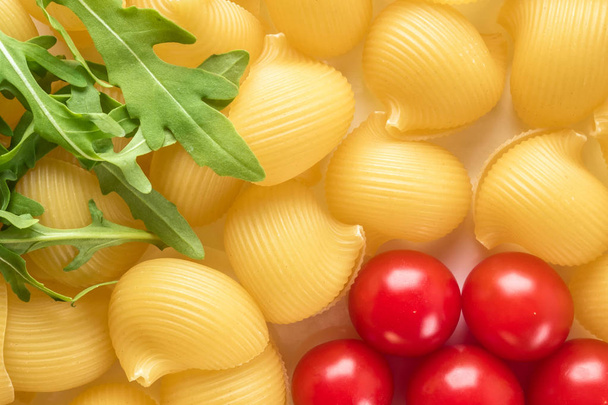 Food background Uncooked Macaroni Lumaconi close-up macro red Cherry Tomatoes in flower form and leaves Rucola Salad Concept set of ingredients for Pasta - Zdjęcie, obraz