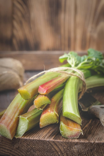 Stems of fresh young rhubarb with kitchen knife on cutting board Ingredients for food recipes healthy diet detox organic food vegetables on wooden background, low key copy space top view soft focus - Fotoğraf, Görsel