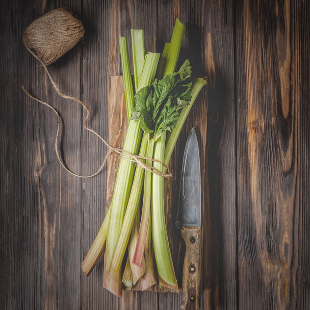 Stems of fresh young rhubarb with kitchen knife on cutting board Ingredients for food recipes healthy diet detox organic food vegetables on wooden background, low key copy space top view soft focus - Fotoğraf, Görsel