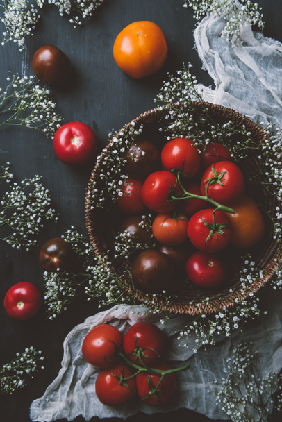 top view of fresh red tomatoes in wicker bowl with white flowers - Φωτογραφία, εικόνα