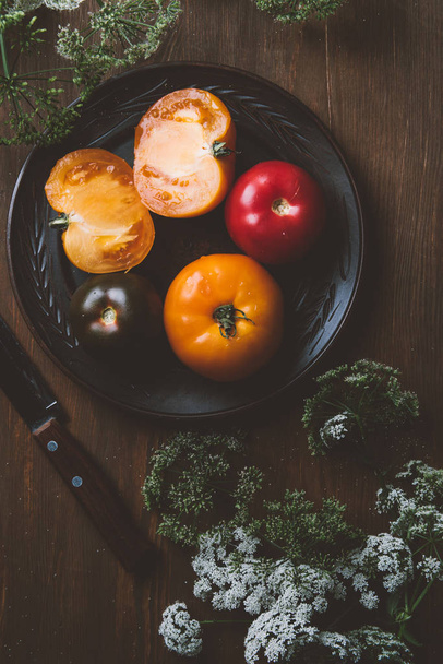Widok z góry pomidorów na płytę ceramiczną z nożem i pietruszka kwiaty - Zdjęcie, obraz