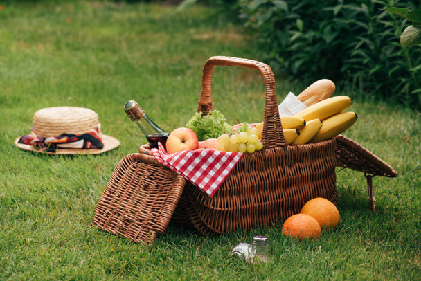вкусные фрукты и бутылка шампанского в плетеной корзине на зеленой траве на пикнике
 - Фото, изображение