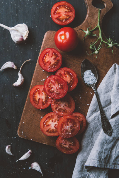 top view of red organic tomatoes, garlic and salt in spoon on cutting board - Φωτογραφία, εικόνα