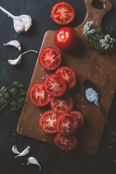top view of ripe red tomatoes, garlic, flowers and salt on cutting board - Fotó, kép