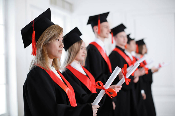Students in bachelor robes with diplomas indoors. Graduation day - Photo, Image