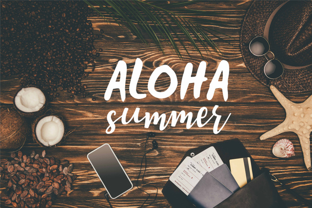 top view smartphone and flight tickets surrounded with various tropical travel attributes on wooden surface with "Aloha summer" lettering  - Foto, Bild