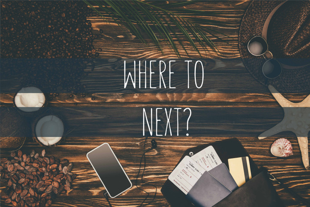 bovenaanzicht smartphone en vlucht tickets omgeven met verschillende tropische reizen kenmerken van houten ondergrond met "waar volgende?" belettering  - Foto, afbeelding