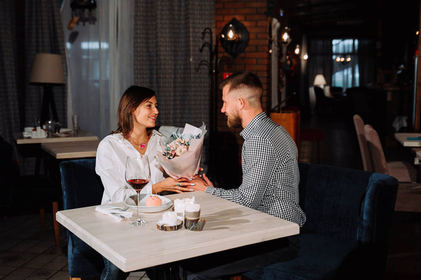 Surprise Beautiful romantic couple in cafe. Young man is presenting flowers to his beloved. Feel of happiness. - Foto, Imagem