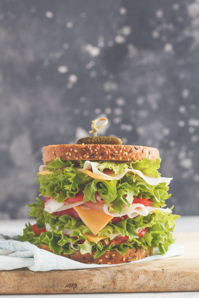 Big sandwich with meat, cheese and fresh vegetables on a wooden board, dark background. - Fotó, kép