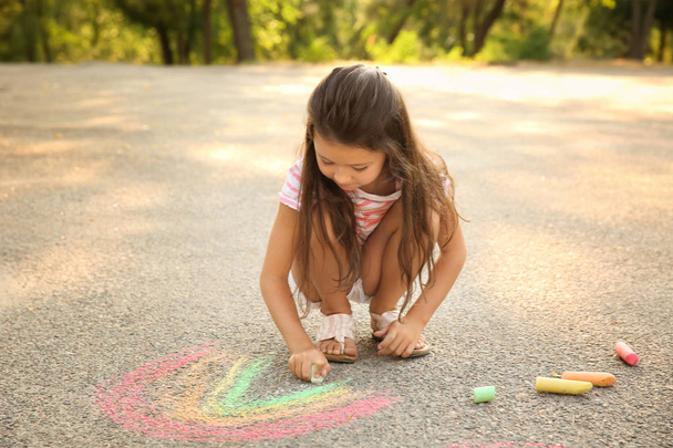 Cute little girl drawing with chalk on asphalt, outdoors - 写真・画像