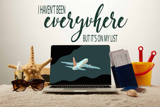 close up view of laptop with inspection and airplane illustration, sea star, sunglasses, passports with tickets and toy bucket on sand on grey background  - Photo, Image