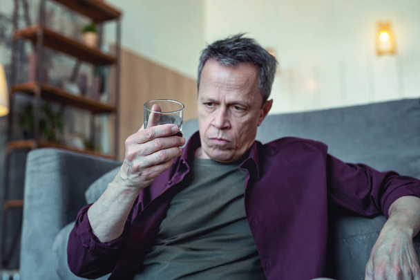 Depressed man looking at glass of vodka - Foto, Imagen