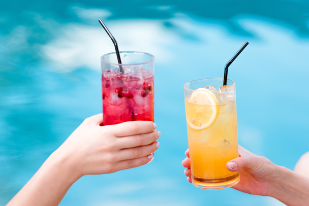 περικοπεί shot των γυναικών που τσούγκριζαν ποτήρια γευστικότατα cocktails μπροστά από την πισίνα - Φωτογραφία, εικόνα