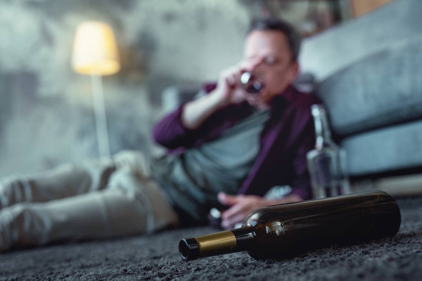 Bottle of cognac lying on the floor near drunk man - Fotó, kép