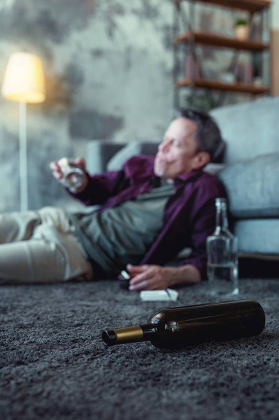 Cognac bottle lying near alcohol addicted husband - Foto, afbeelding