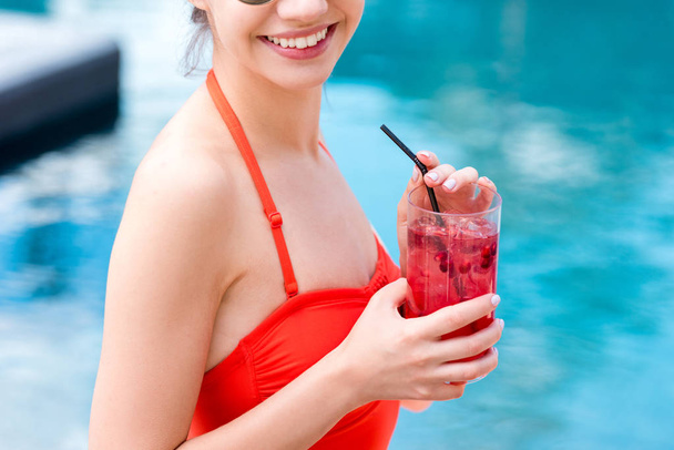 Schnappschuss einer lächelnden jungen Frau mit Beerencocktail am Pool - Foto, Bild