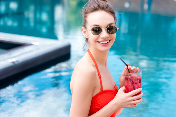 happy young woman in vintage sunglasses with berry cocktail at poolside - Photo, Image