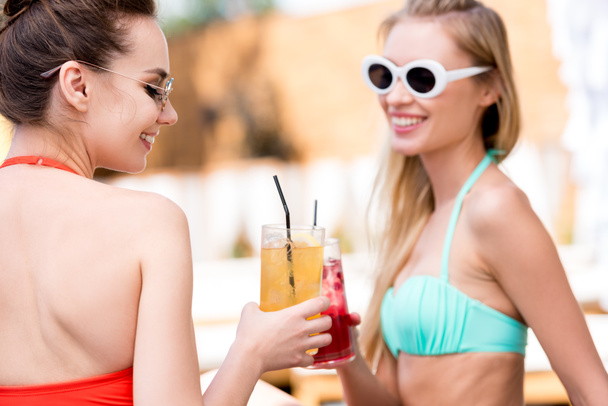 счастливые молодые женщины звонят стаканы коктейлей у бассейна
 - Фото, изображение