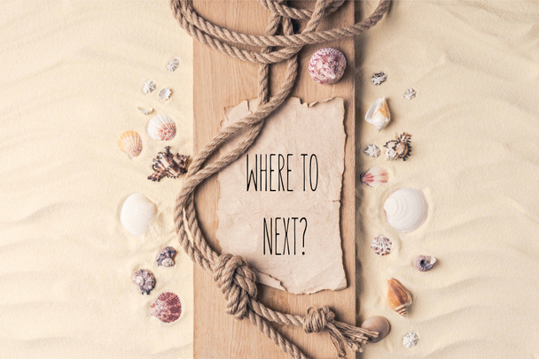 Summer travel template with seashells and rope on wooden pier on light sand with "where to next?" lettering - Photo, Image