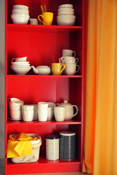 Red storage stand with ceramic dishware indoors - Фото, изображение