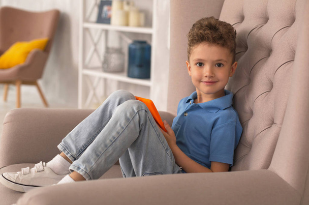 Curly handsome boy sitting in armchair at home - Φωτογραφία, εικόνα