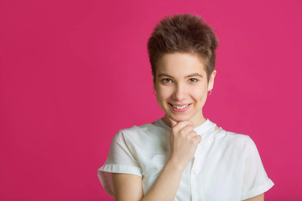 beautiful young girl with short hairdo in a white t-shirt on a pink background - Foto, afbeelding