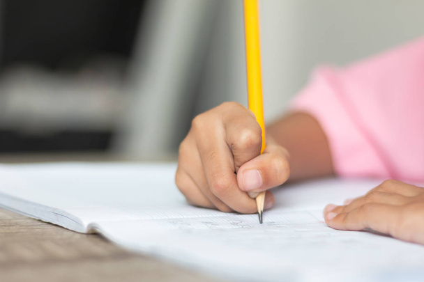 Nahaufnahme eines kleinen Mädchens, das Hausaufgaben macht. Hand hält einen gelben Bleistift und schreibt in ein Notizbuch. Schärfentiefe und unscharfen Hintergrund mit Kopierraum auswählen. - Foto, Bild