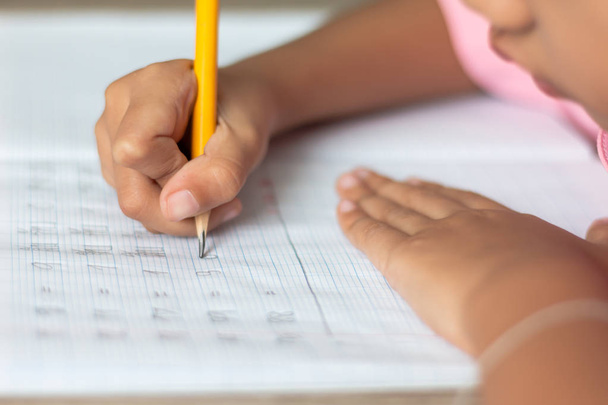 Nahaufnahme eines kleinen Mädchens, das Hausaufgaben macht. Hand hält einen gelben Bleistift und schreibt in ein Notizbuch. Schärfentiefe und unscharfen Hintergrund auswählen. - Foto, Bild