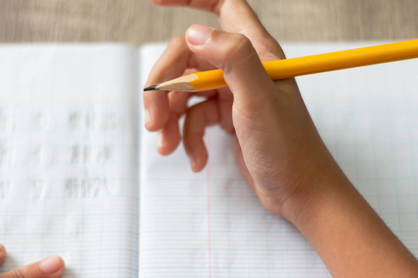 Una niña haciendo los deberes. La mano sostiene un lápiz amarillo con ángulo alto. Seleccione la profundidad de campo superficial de enfoque y el fondo borroso
. - Foto, Imagen