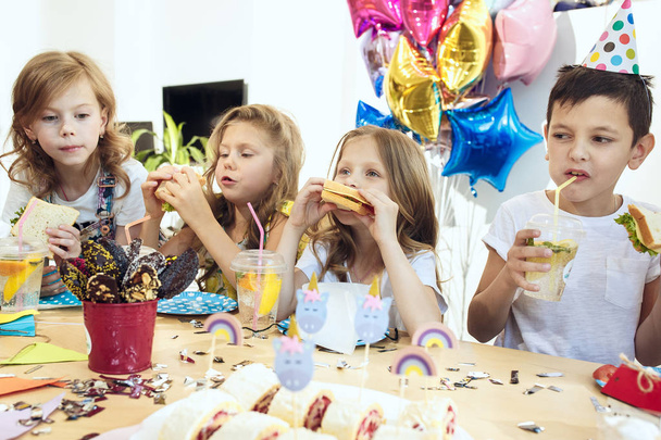 Діти та прикраси на день народження. Хлопчики та дівчатка за столом з їжею, тортами, напоями та вечірніми гаджетами
. - Фото, зображення