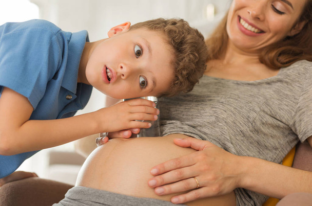 Curious dark-eyed boy listening to pregnant tummy - Foto, imagen