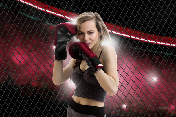 Gorgeous young blonde mma fighter in a red corner of the cage looking at the camera - Foto, Bild