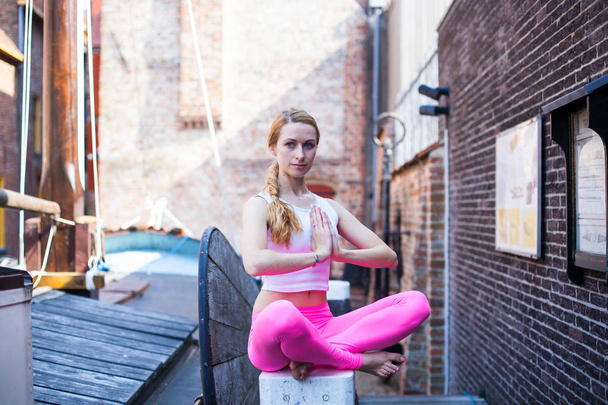Retrato menina ioga loira na cidade da manhã Groningen, mulher com cabelo loiro longo meditando e fazendo exercícios de ioga na rua da cidade, conceito de estilo de vida saudável
 - Foto, Imagem