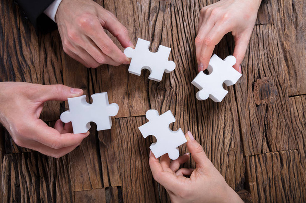 Group Of Businesspeople Solving Jigsaw Puzzle On Desk - Fotografie, Obrázek