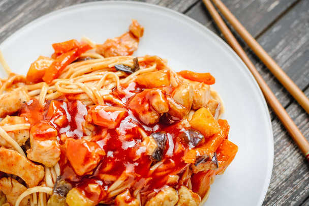 Udon ανακατεύετε τηγανητά noodles με κοτόπουλο και λαχανικά στο πιάτο και chopsticks σε μαύρο φόντο ξύλινη - Φωτογραφία, εικόνα
