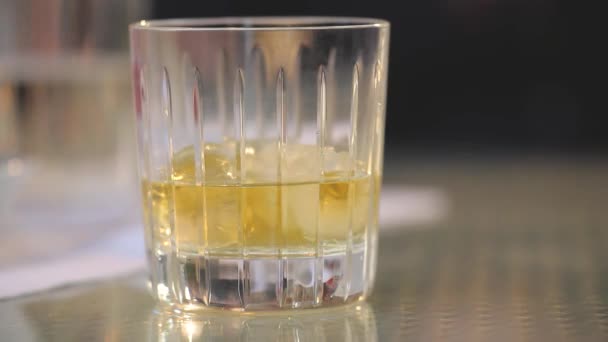 The man takes a glass of whiskey with ice from the table, puts a glass of whiskey with ice on the table, close-up, shallow depth of field, Glasses of whiskey in businessmans hands on wooden table - Felvétel, videó