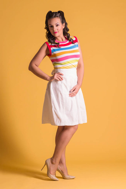 Smiling woman in skirt with hairdo stands in yellow studio, pin up style, full body - Foto, imagen