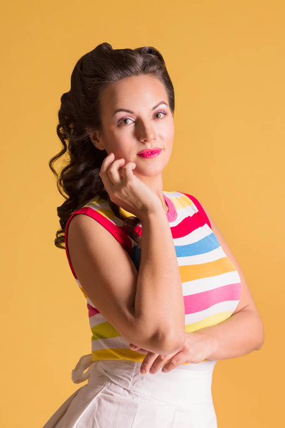 Young woman in striped shirt, with hairdo stands in yellow studio, pin up style - Photo, Image