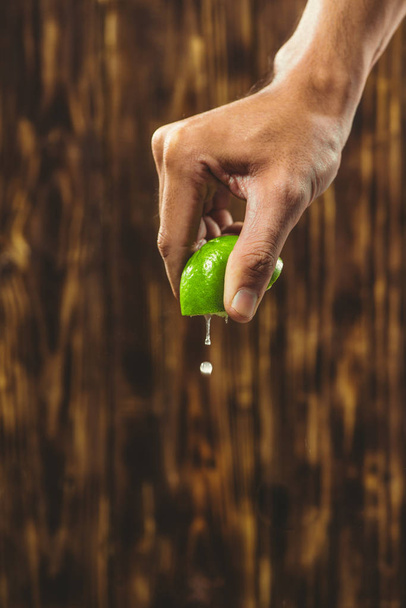 Hand squeeze lime with lime drop on wooden background - Photo, Image