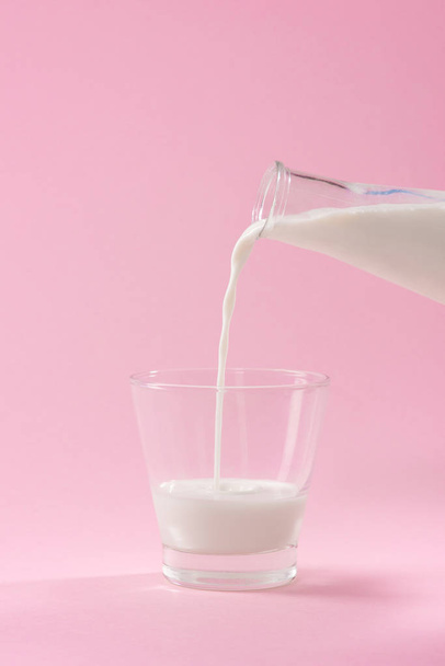 Milch in Glas auf rosa Hintergrund gießen - Foto, Bild