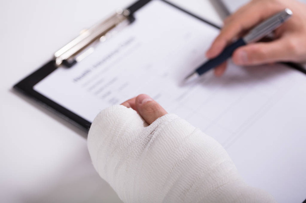 High Angle View Of A Person With Fractured Hand Filling Health Insurance Form - Foto, Imagen