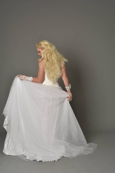 Pełna długość Portret Blondynka dziewczyna ubrana w białą suknię, stojący poza z powrotem do aparatu. studio szary tło. - Zdjęcie, obraz