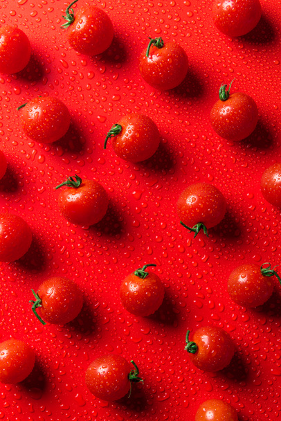 bovenaanzicht van patroon van cherry tomaten op rode ondergrond met water druppels - Foto, afbeelding