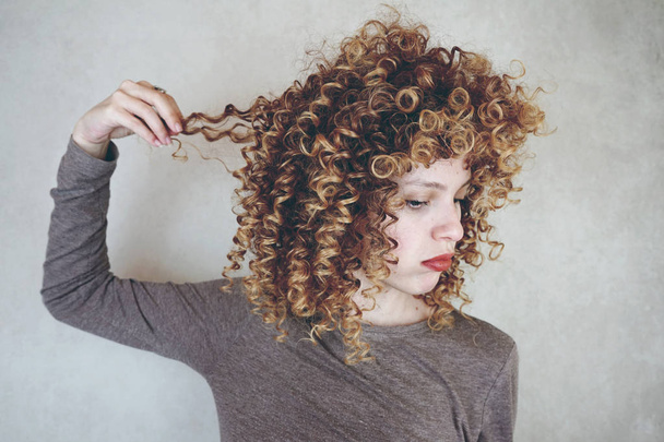 Фото молодой милые женщины с вьющимися волосами на фоне серой стене - Фото, изображение