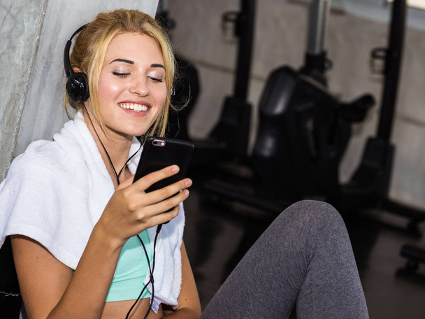 Genç sportwoman spor salonunda müzik dinleme için Smartphone kullanarak - Fotoğraf, Görsel