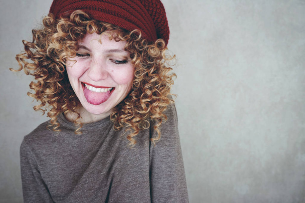 photo of young cute woman with curly hair and red hat on grey wall background - Photo, Image