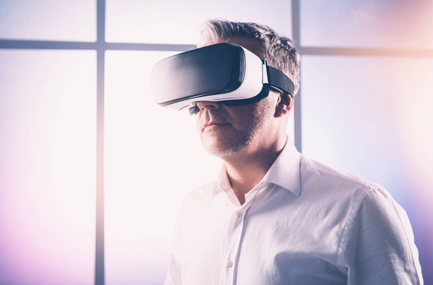 Mature man experiencing virtual reality, he is wearing a VR headset, technology and innovation concept - Photo, image