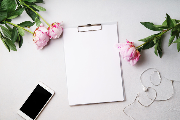  feminine desk workspace with empty blank clipboard and smartphone with pink peony flowers,  top view - Foto, Bild