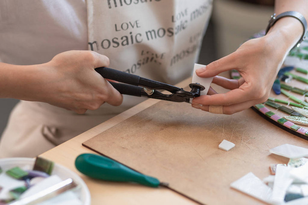 Local de trabalho do mestre do mosaico: mãos das mulheres segurando ferramenta para detalhes do mosaico no processo de fazer um mosaico
 - Foto, Imagem